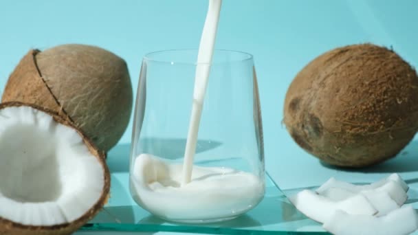 ココナッツミルクは青い背景にココナッツの間にガラスに注ぎ ゆっくりとした動き — ストック動画