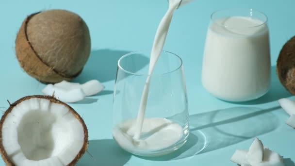 ココナッツミルクは青い背景にココナッツの間にガラスに注ぎ ゆっくりとした動き — ストック動画