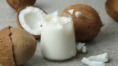 Hindistan cevizi dilimleri yavaş çekimde bir bardak hindistan cevizi sütüne dökülüyor..