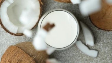 Hindistan cevizi dilimleri bir bardak hindistan cevizi sütüne dökülüyor, yavaş çekim, üst görüntü.