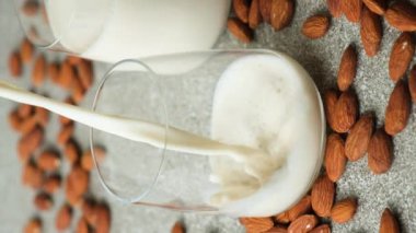 Gri arka planda bir bardağa badem sütü dökülüyor, dikey ağır çekim