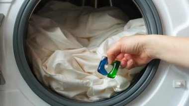 Birisi çamaşır makinesinin variline çamaşır kapsülü atıyor.