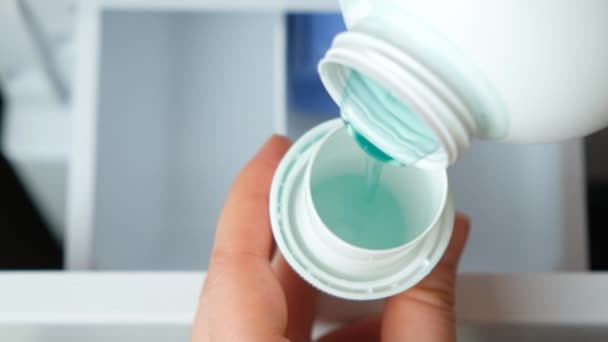 在洗涤剂洗衣机打开的罐体的背景下 液体凝胶倒入瓶盖 — 图库视频影像