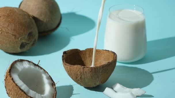 青い背景にココナッツシェルに注ぐ健康的なビーガンココナッツミルク スローモーション — ストック動画