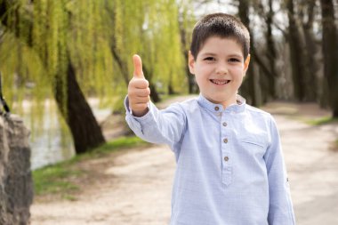 Altı yaşında bir çocuk bahar parkında yürürken başparmağını kaldırıyor ve gülümsüyor..