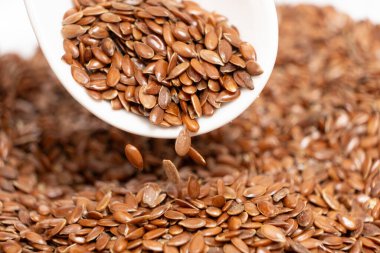 Çiğ keten tohumları kaşıktan tabak makrosuna dökülüyor..