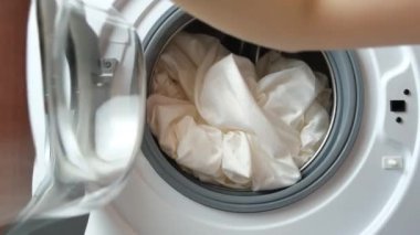 Kadın çamaşır makinesinden temiz çamaşırları çıkarıp kapıyı açıyor.