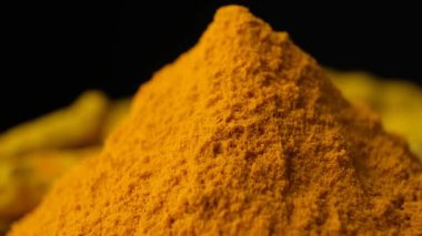 Siyah arkaplanda yavaşça dönen zerdeçal tozunun makro görüntüsü.