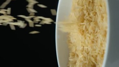 Uzun buğday haşlanmış basmati pilavı siyah zemin üzerine dökülüyor, dikey yavaş çekim.