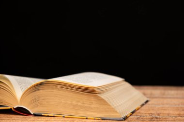 Ahşap ve siyah arka plan üzerine açık bir kitap. Nesillerin bilgeliği, bilgi ve okuma sevgisi, yazma yeri.