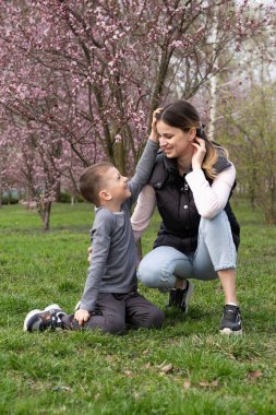 Mutlu anne ve küçük oğul. Çiçek açan bahçedeki ortaokul çocuğu. Kiraz çiçeklerinin arasında.