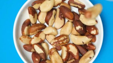 Brezilya fıstıkları tabağa dökülüyor, yavaş çekim, mavi arkaplan.