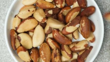 Brezilya fıstıkları tabağa dökülüyor, yavaş çekim, gri arkaplan.