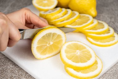 Taş mutfak tahtasının üzerinde keskin bir bıçakla limonu dilimlere ayıran kadın.