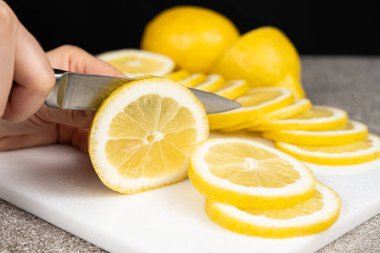 Taş mutfak tahtasının üzerinde keskin bir bıçakla limonu dilimlere ayıran kadın.