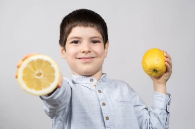 A happy six-year-old boy holds lemons in his hands and smiles. clipart