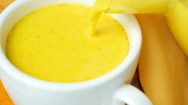 Altın süt bardağa doluyor, ağır çekimde. Zerdeçal ile geleneksel Ayurvedic içecek