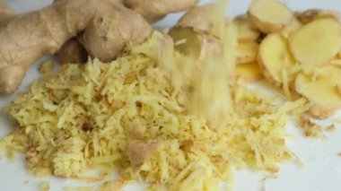 Güzelce rendelenmiş zencefil kökü parçaları mutfak tahtasına yavaş çekimde düşer.