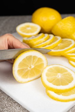 Taş mutfak tahtasının üzerinde keskin bir bıçakla limonu dilimlere ayıran kadın.