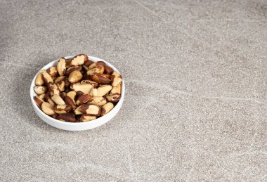 Brazil nuts in plate on grey background, copy space for text.