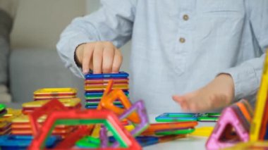 Çocuk bir manyetik yapıcıyla oynuyor, masada otururken çeşitli figürler oluşturuyor.