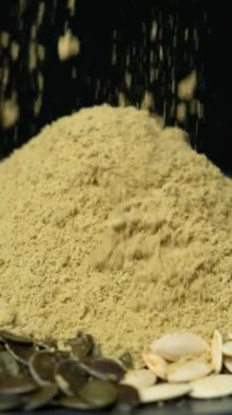 Yer kabağı çekirdekleri, balkabağı unu siyah arka plana dökülüyor, dikey yavaş çekim