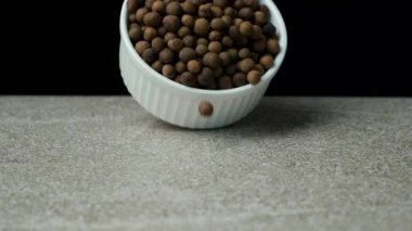 Siyah arka planda taş masaya dökülen siyah biberler, yavaş çekim.