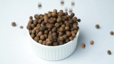 Siyah biberler beyaz arka planda bir tabağa dökülüyor, ağır çekimde.