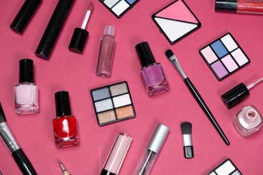 Pembe arka planda çeşitli dekoratif kozmetik ürünleri ve fırçalar.