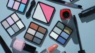 Mavi arka planda çeşitli dekoratif kozmetik ürünleri ve fırçalar.