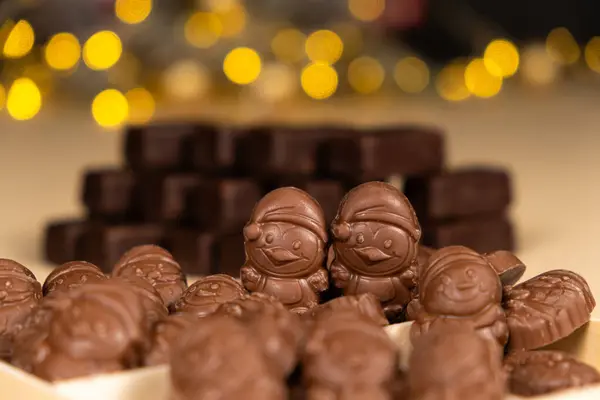 stock image Chocolates in the shape of Christmas figures on the background of a flashing garland.