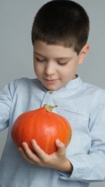 Mutlu çocuk sağlıklı bir balkabağı tutuyor ve beyaz bir arka planda gülümsüyor..