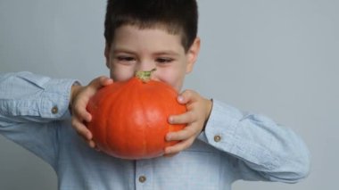 Mutlu çocuk sağlıklı bir balkabağı tutuyor ve beyaz bir arka planda gülümsüyor.