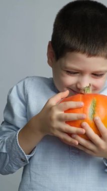 Mutlu çocuk sağlıklı bir balkabağı tutuyor ve beyaz bir arka planda gülümsüyor.