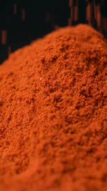 Baharatlı tütsülenmiş kırmızı biber dikey siyah arkaplana makro dökülüyor