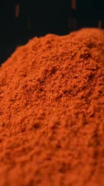 Baharatlı tütsülenmiş kırmızı biber dikey siyah arkaplana makro dökülüyor