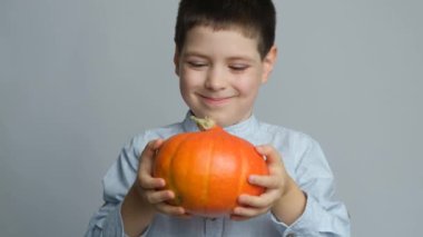 Mutlu çocuk sağlıklı bir balkabağı tutuyor ve beyaz bir arka planda gülümsüyor..