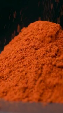 Baharatlı tütsülenmiş kırmızı biber dikey siyah arkaplana makro dökülüyor