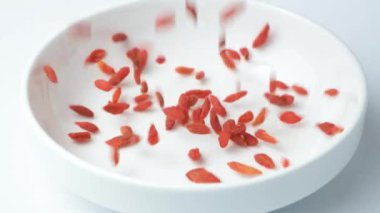 Goji Berries Tibet böğürtlenleri kurutulmuş süper yiyecekler uzun ömürlü meyveler yavaş çekimde bir tabağa dökülüyor..