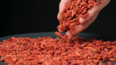 Siyah arka planda yavaş çekimde kurumuş goji üzümleri döküyorum..