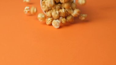 Tatlı karamelli patlamış mısır camdan dökülüyor, turuncu arka plan, yavaş çekim