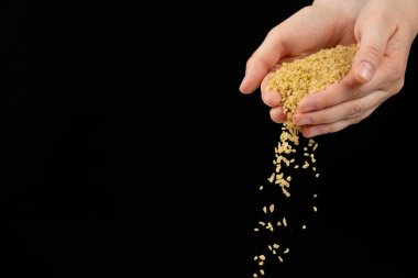 Eller, metin için siyah arkaplan boşluğuna çiğ bulgur gevrekleri döküyor.