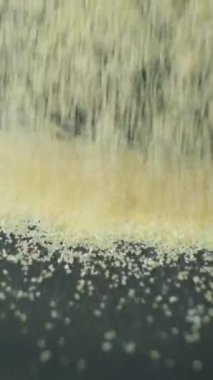 Pişmemiş irilmiş irmik gevreği siyah arka planda dikey yavaş çekime dökülüyor.