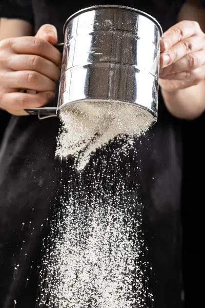 Aşçı buğday ununu bir metal süzgecinden geçirir..