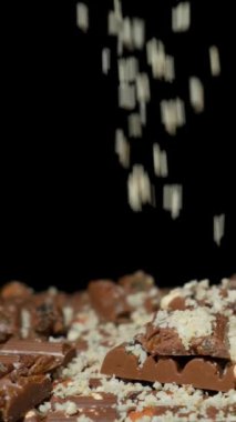 Çikolataya dökülen rendelenmiş fındık ezmesi, siyah arka plan, dikey yavaş çekim.