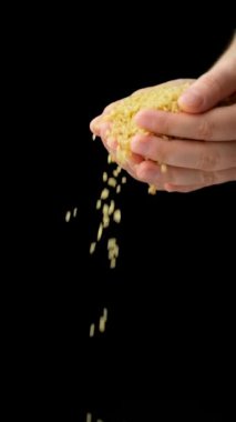 Eller çiğ bulgur gevreğini siyah arka planda, dikey yavaş çekimde döküyor.