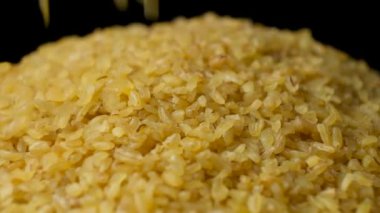 Pişmemiş bulgur buğday dökülmüş. Siyah arkaplanda makro yavaş çekim.