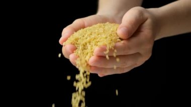Eller çiğ bulgur gevreğini siyah arka plana döküyor, yavaş çekim.