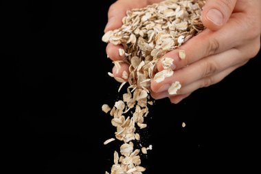 Eller, siyah bir zemine çiğ yulaf ezmesi döküyor.