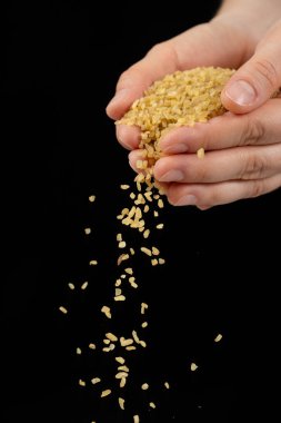 Çiğ bulgur gevreği döken eller siyah arka planda buğdayı çatlattı.